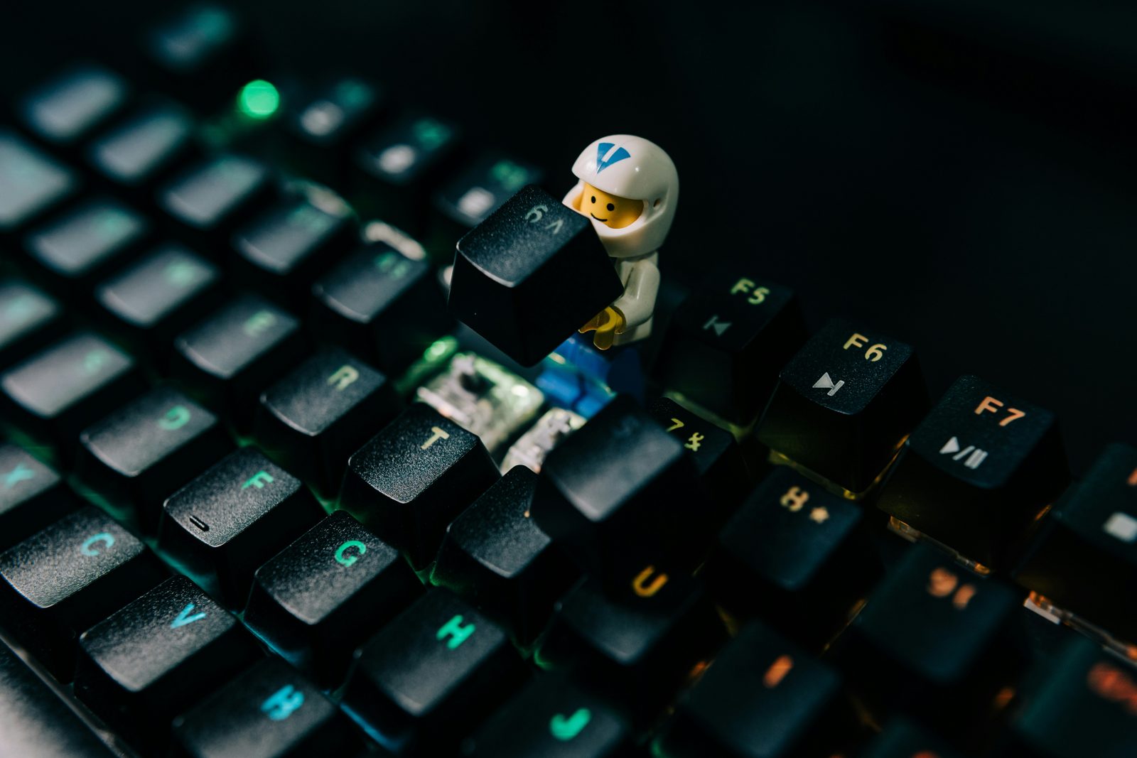 A toy astronaut lifting a key off a backlit mechanical keyboard